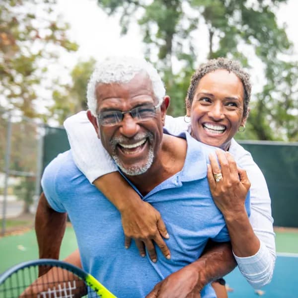 A man and woman smiling holding a tennis racket