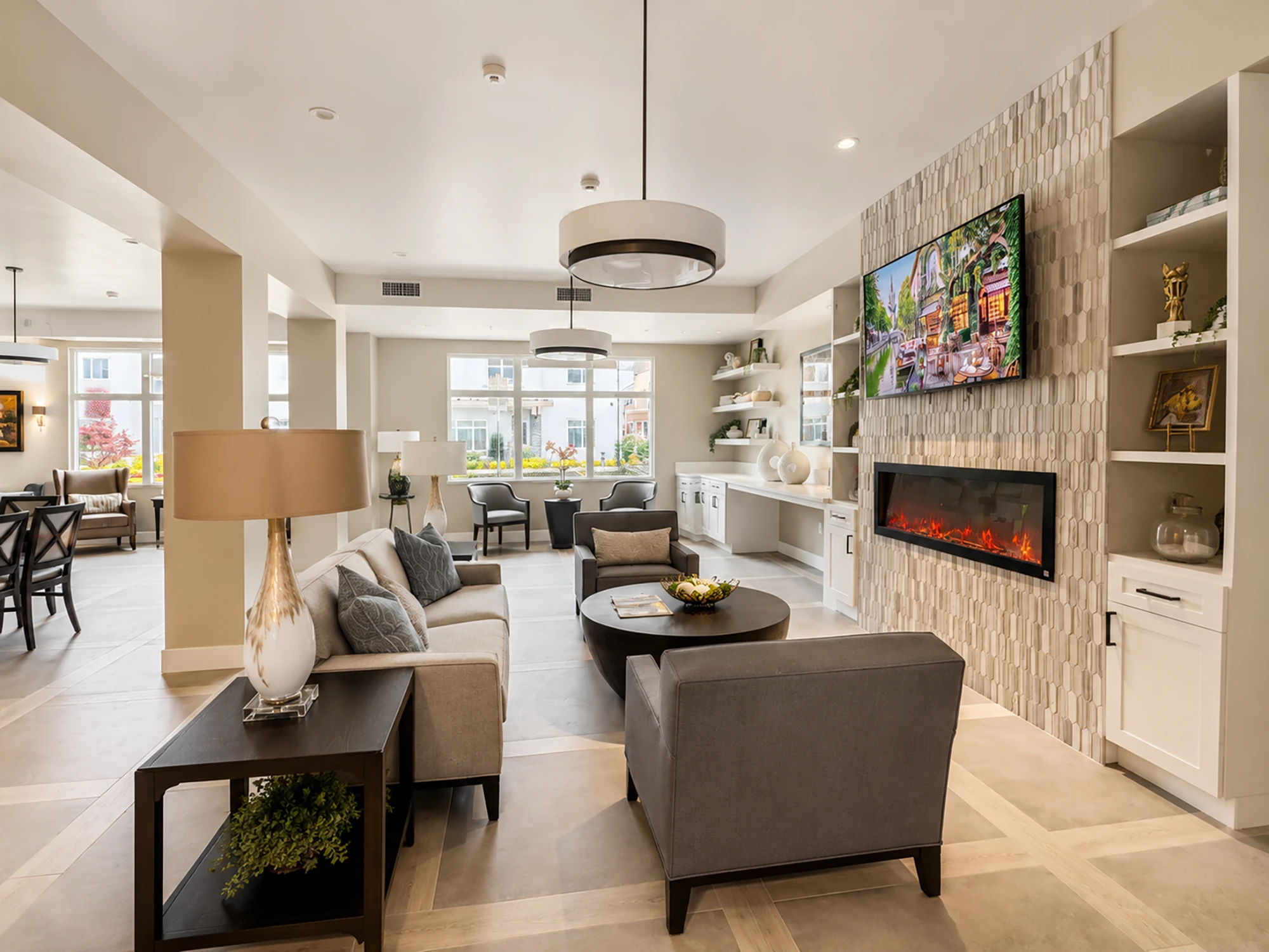 Bright living room with contemporary sofa, armchair, coffee table, wall-mounted TV above built-in electric fireplace, and decorative shelving with plants and books