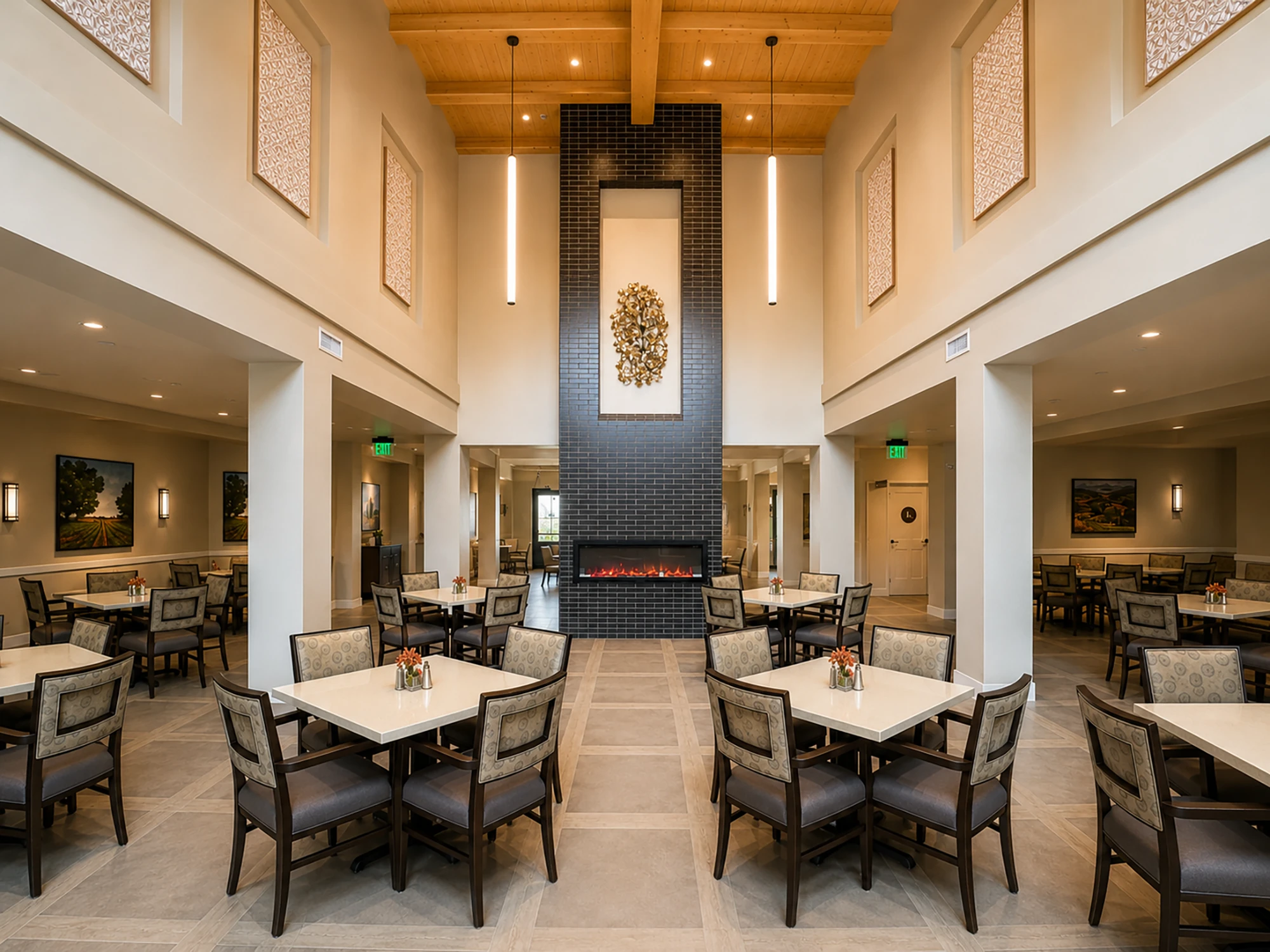 Spacious senior living dining area with tables, chairs, a central black brick fireplace, wooden ceiling, pendant lights, and floral decorations.