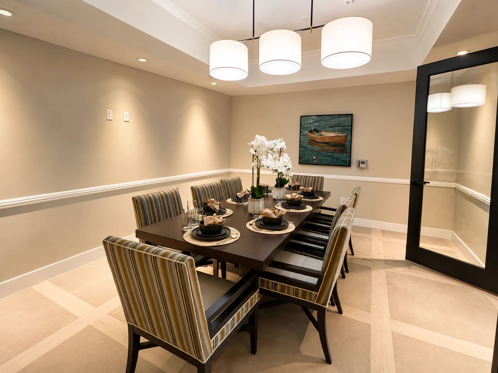 Elegant dining room with a rectangular table set for eight, decorated with white orchids and tableware, featuring a painting and glass door.